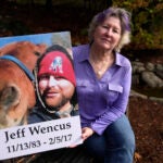 Lynn Wencus, of Wrentham, Mass., holds a photograph of her son Jeff while seated in a garden at her home.