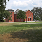A college campus with a green yard in the foreground and red brick buildings in the distance