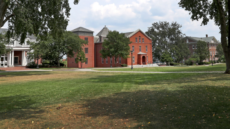 A college campus with a green yard in the foreground and red brick buildings in the distance
