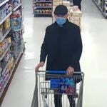 A man wearing a long coat, flat cap and surgical mask inside a Market Basket in Concord, New Hampshire.