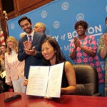 Boston Mayor Michelle Wu shows the executive order she signed that eliminates fossil fuel usage for new construction and major renovations of City buildings. Standing on her right side is Hessann Farooqi, advocacy director at Boston Climate Action Network.