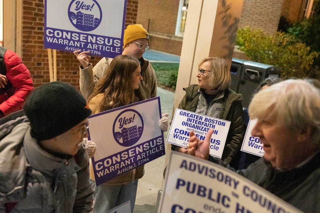 Several people stand outside of Brookline High School with signs promoting the passage of a rezoning proposal.