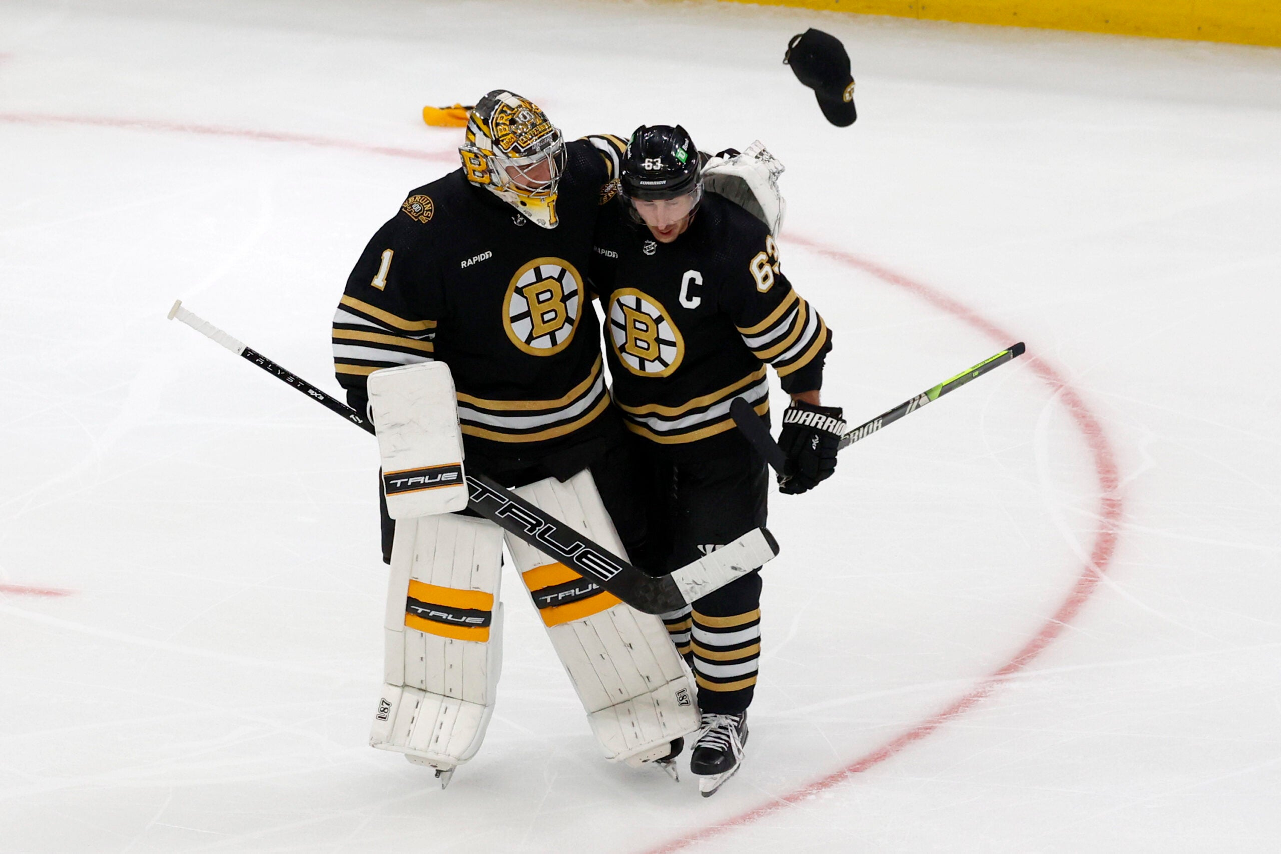 A cap is thrown onto the ice as Boston Bruins goalie Jeremy Swayman (1) congratulates teammate Brad Marchand (63) after Marchand scored his third goal for a hat trick during the third period of an NHL hockey game against the Columbus Blue Jackets, Sunday, Dec. 3, 2023, in Boston.