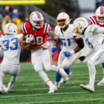 New England Patriots running back Rhamondre Stevenson (38) escapes the grasp of Los Angeles Chargers cornerback Deane Leonard (33) and evades Los Angeles Chargers cornerback Deane Leonard (33) during the first half of an NFL football game on Sunday, Dec. 3, 2023, in Foxborough, Mass.