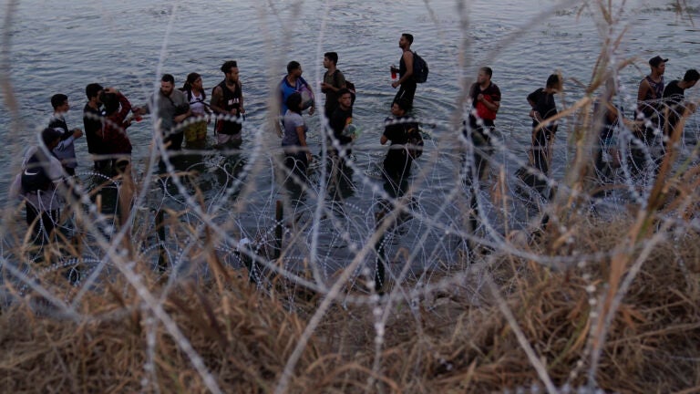FILE - Migrants wait to climb over concertina wire after they crossed the Rio Grande and entered the U.S. from Mexico, Saturday, Sept. 23, 2023, in Eagle Pass, Texas.