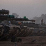 Israeli soldiers stand on top of a tank in a staging area at the Israeli-Gaza border in southern Israel, Monday, Jan. 1, 2024.