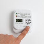 white carbon monoxide alarm finger is pressing button