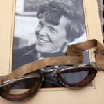 An original, unpublished personal photo of Amelia Earhart dated 1937, along with goggles she was wearing during her first plane crash.