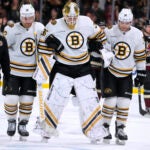 An injured Boston Bruins goaltender Linus Ullmark (35) is helped off the ice by defenseman Kevin Shattenkirk (12), left wing Jake DeBrusk (74) and a member of the training staff during overtime of the team's NHL hockey game against the Arizona Coyotes on Tuesday, Jan. 9, 2024, in Tempe, Ariz. The Coyotes won 4-3.
