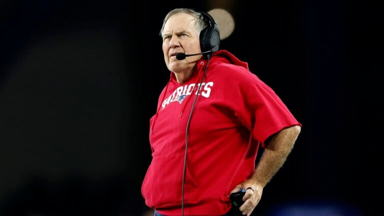 New England Patriots head coach Bill Belichick wearing a red New England Patriots hoodie with cutoff sleeves.
