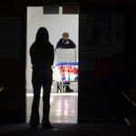 A first-time voter waits in the doorway for a voting booth as another voter completes his ballot.
