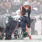 New England Patriots quarterback Bailey Zappe (4) evades being sacked by New York Jets defensive tackle Quinnen Williams (95) with the help of offensive tackle Vederian Lowe (59) during the first half of an NFL football game on Sunday, Jan. 7, 2024, in Foxborough, Mass.