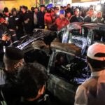 People, rescuers, and security forces gathered around a vehicle hit by a drone strike, reportedly killing three people, including two leaders of a pro-Iran group, in Baghdad on Feb. 7.