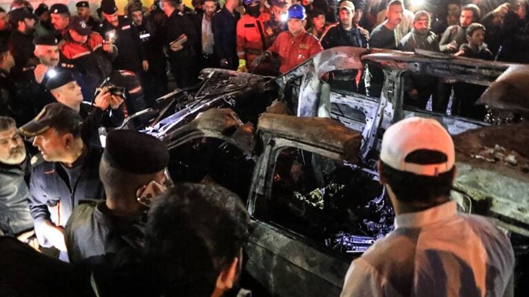 People, rescuers, and security forces gathered around a vehicle hit by a drone strike, reportedly killing three people, including two leaders of a pro-Iran group, in Baghdad on Feb. 7.