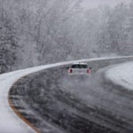 A white vehicle drives down a road as snow falls.