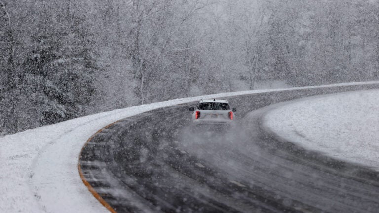 A white vehicle drives down a road as snow falls.