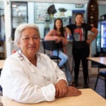 Sherry Pocknett sits at her restaurant, Sly Fox Den Too, while her two daughters sit in the background.