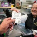 Dot Skoko, owner of Dot's Dollar More or Less shop in Mt. Lebanon, Pa., hands a customer a Mega Millions lottery ticket.