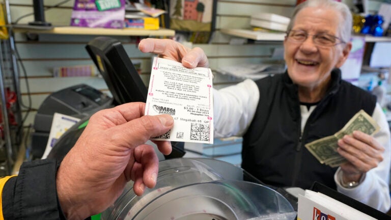 Dot Skoko, owner of Dot's Dollar More or Less shop in Mt. Lebanon, Pa., hands a customer a Mega Millions lottery ticket.