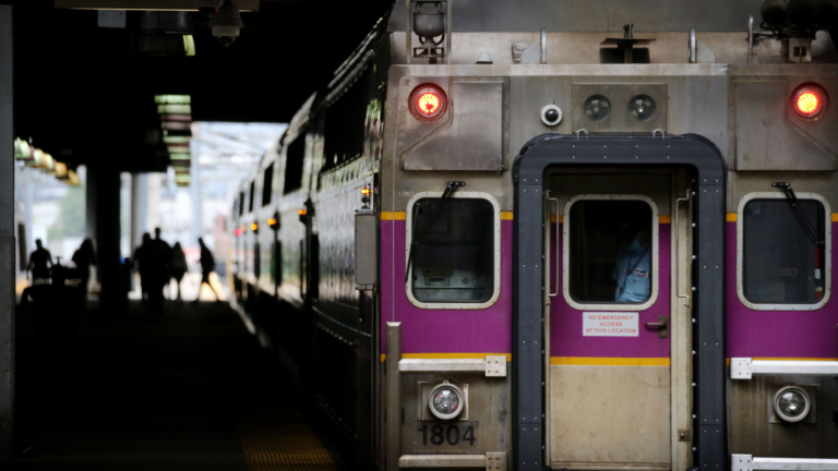 A Commuter Rail train parked alongside a train platform with commuters walking in the background