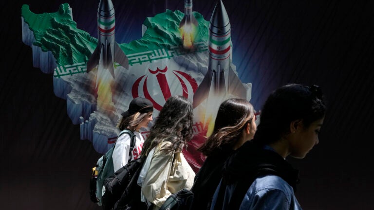 Iranian women without wearing their mandatory Islamic headscarf walk past a banner showing missiles being launched from Iranian map in northern Tehran, Iran.