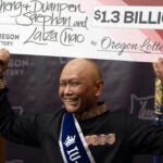 Cheng "Charlie" Saephan holds a check above his head at the Oregon Lottery headquarters.