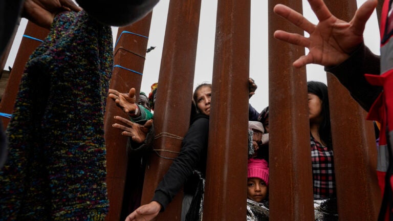 Migrants reach through a border wall for clothing handed out by volunteers as they wait between two border walls to apply for asylum in San Diego.