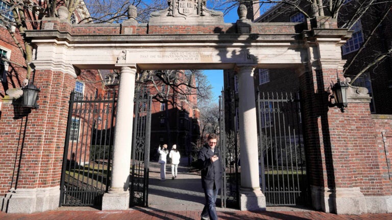 A passer-by walks through a gate to the Harvard University campus in Cambridge, Mass.