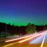Northern lights or aurora borealis illuminate the night sky along a highway north of San Francisco in Middletown, California.