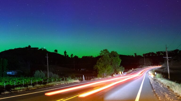 Northern lights or aurora borealis illuminate the night sky along a highway north of San Francisco in Middletown, California.