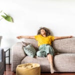 Happy woman relaxing on the sofa at home - Smiling girl enjoying day off lying on the couch - Healthy life style, good vibes people and new home concept renting