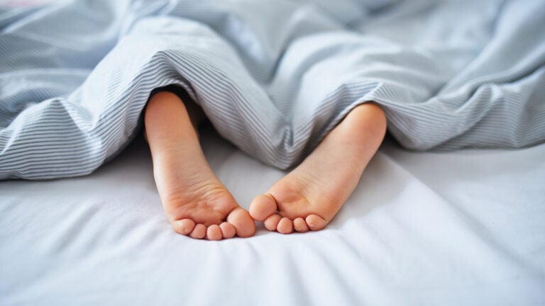Little child's feet in bed covered with blanket. Kid sleeping in a comfortable bed. Early morning at home