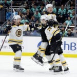 Boston Bruins defenseman Matt Grzelcyk, left, Charlie McAvoy, top, and a teammate celebrate a goal by left wing Jake DeBrusk (74) against the Seattle Kraken during the third period of an NHL hockey game Thursday, Feb. 23, 2023, in Seattle. The Bruins won 6-5.