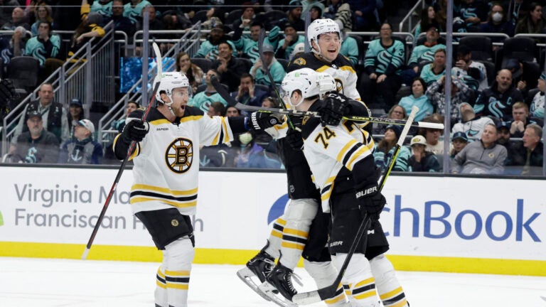 Boston Bruins defenseman Matt Grzelcyk, left, Charlie McAvoy, top, and a teammate celebrate a goal by left wing Jake DeBrusk (74) against the Seattle Kraken during the third period of an NHL hockey game Thursday, Feb. 23, 2023, in Seattle. The Bruins won 6-5.