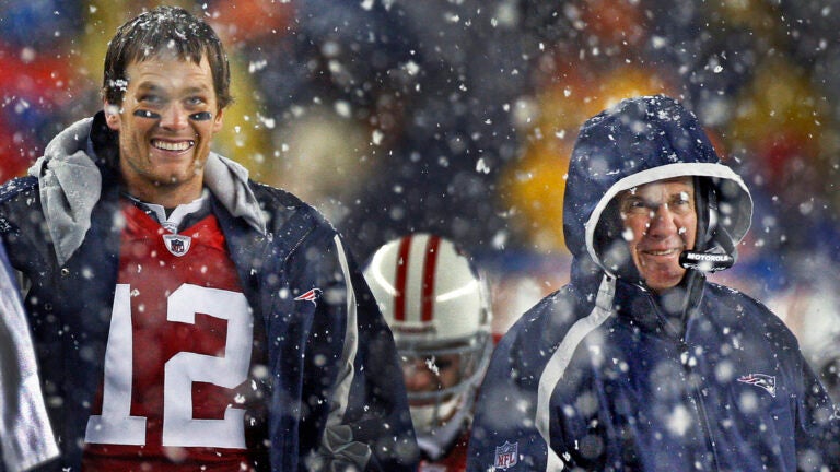 As snow falls around them, Patriots starting quarterback Tom Brady (left) and head coach Bill Belichick (right) laugh as they watch the replay on the scoreboard of the celebration technique of backup quarterback Brian Hoyer (8, backround between them) following his third quarter touchdown. The New England Patriots vs. the Tennessee Titans at Gillette Stadium.