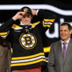 Dean Letourneau, center, adjusts his cap after being selected by the Boston Bruins during the first round of the NHL hockey draft Friday, June 28, 2024, in Las Vegas.