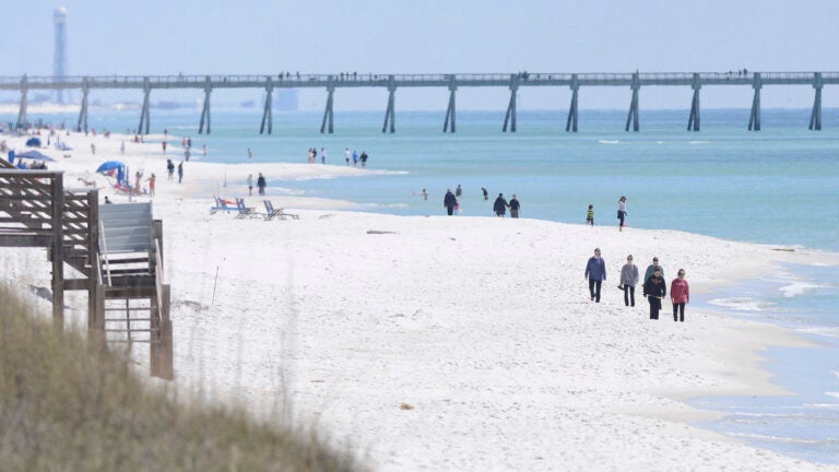 FILE - People walk along the shoreline in Navarre Beach, Fla., on Wednesday March 27, 2013. Authorities are warning of shark dangers this weekend along Florida’s Gulf Coast, where three people were hurt in two separate shark attacks Friday, June 7, 2024.