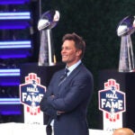 QB Tom Brady smiles as he stands on the stage in front of Superbowl trophies. Former New England Patriots quarterback Tom Brady was inducted into the Patriots Hall of Fame during a ceremony at Gillette Stadium.