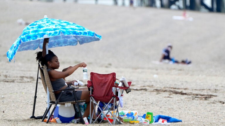 Sierra Payne, of Boston, reaches for a bottle of water while trying to stay cool under an umbrella as she visits Wollaston Beach.