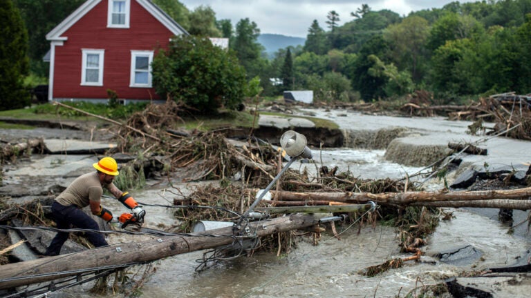 Zac Drown, of Lyndon Electric Company, clears debris amid flood damage in Lyndon, Vt.