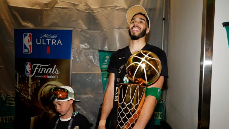 Boston Celtics forward Jayson Tatum holds the Larry O'Brien championship trophy in the locker room with his son Deuce after winning the 2024 NBA Finals over the Dallas Mavericks at TD Garden on Monday, June 17, 2024.