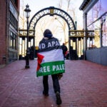 A man wears a Palestinian flag as he walks through an area where a pro-Palestinian encampment had been set up before it was dismantled by police at Emerson College in Boston, on Thursday, April 25, 2024.