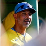 Alex Cora looks up in the dugout in his blue Red Sox hat and yellow Red Sox jersey.