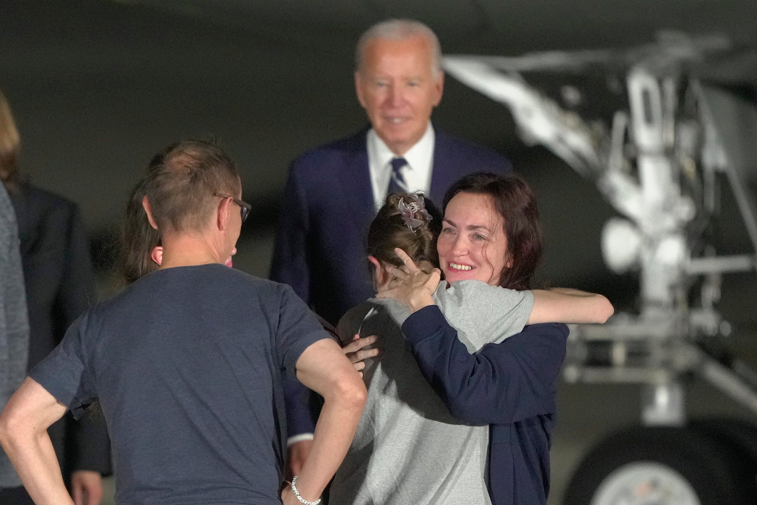 President Joe Biden looks on as Alsu Kurmasheva hugs a family member on the tarmac after arriving at Andrews Air Force Base, Md.