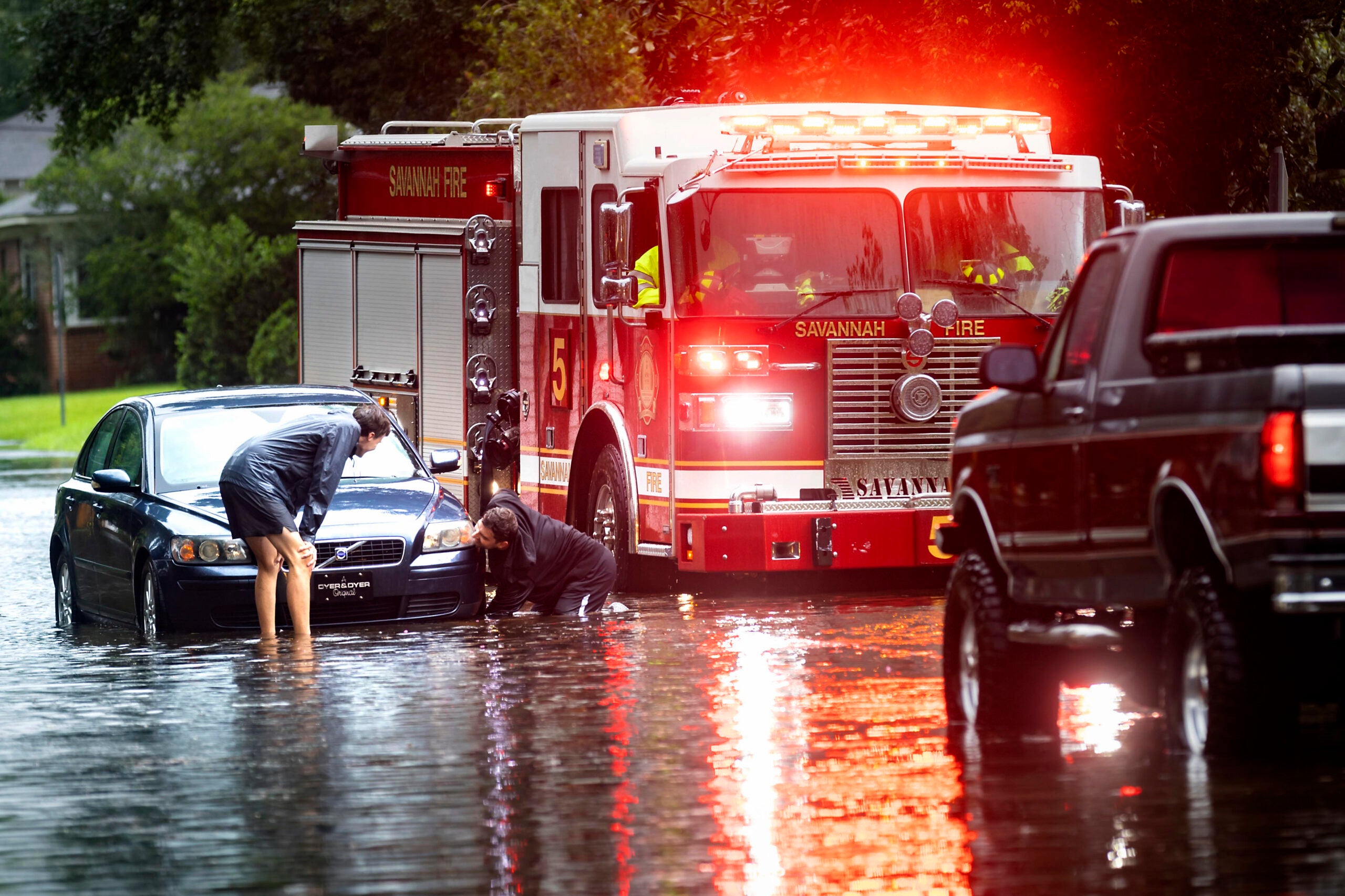 People attach a towline to a stranded vehicle on a flooded street after heavy rain from Tropical Storm Debby.