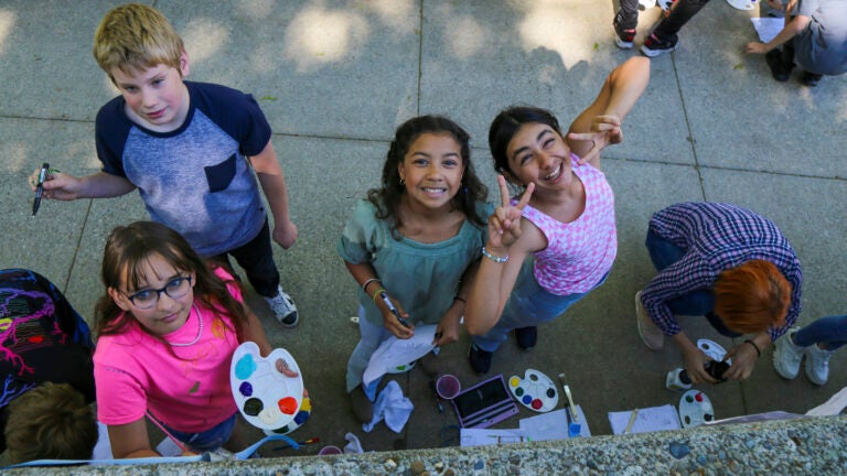 This photo provided by Spokane Public Schools shows Adams Elementary fifth graders pausing to pose for a photo while painting a mural at Spokane Community College, May 2024, in Spokane, Wash.