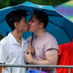 Jon Batayola, left, and Daniel Biginton embrace under an umbrella as they await the beginning of Chicago's annual Pride Parade, June 25, 2023, in Chicago.