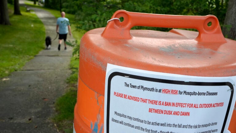 A passer-by walks a dog along a walkway, in Plymouth, Mass.