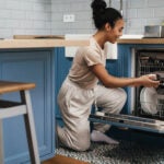 Happy black woman smiling while using dishwasher at home kitchen