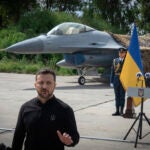 Ukraine's President Volodymyr Zelenskyy answers media questions standing against the background of Ukraine's Air Force's F-16 fighter jets in an undisclosed location in Ukraine, Sunday, Aug. 4, 2024.